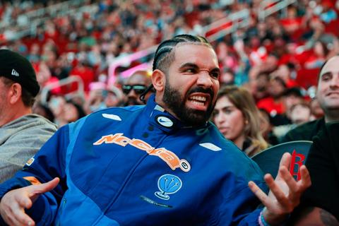 Drake in an arena crowd wearing a blue jacket
