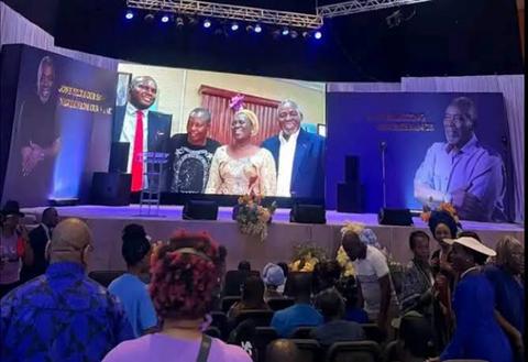 tribute event stage with audience and screen showing Olu Jacobs and Joke Silva