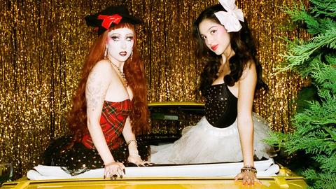two women posing against a gold curtain