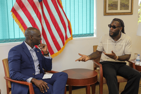 two men talking in an office with a US flag