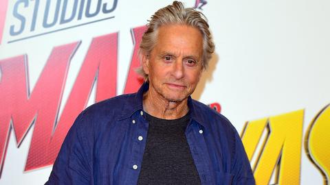 grey-haired man at a photo call, large studio logo backdrop behind him (in-scene signage)