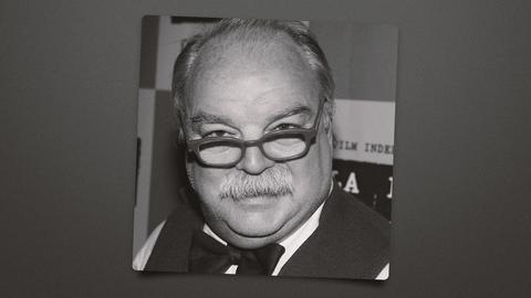 black-and-white portrait of a balding man with glasses and mustache, sign text behind