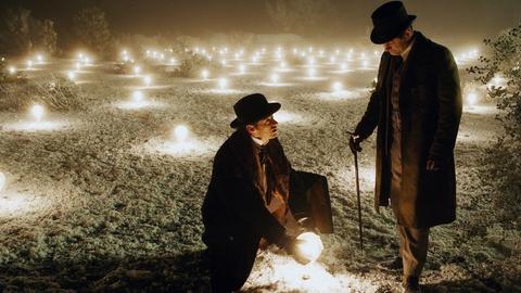 two men in hats and coats in a field of lights