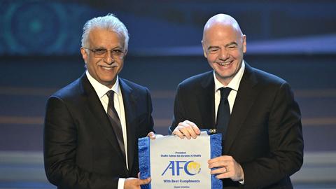 Two officials in suits holding a framed AFC presentation item on stage