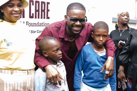 Man in sunglasses and maroon shirt posing with two young boys, a woman in a cream tee at left, foundation banner behind