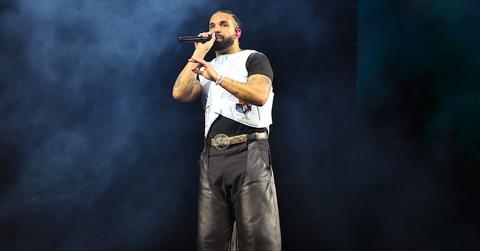 Bearded man in a white vest and black leather trousers performing with a microphone on a smoky stage