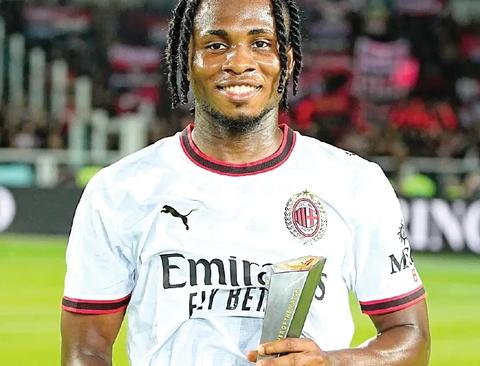Smiling player in Milan's white away kit holding an award plaque; clean portrait, no overlay text