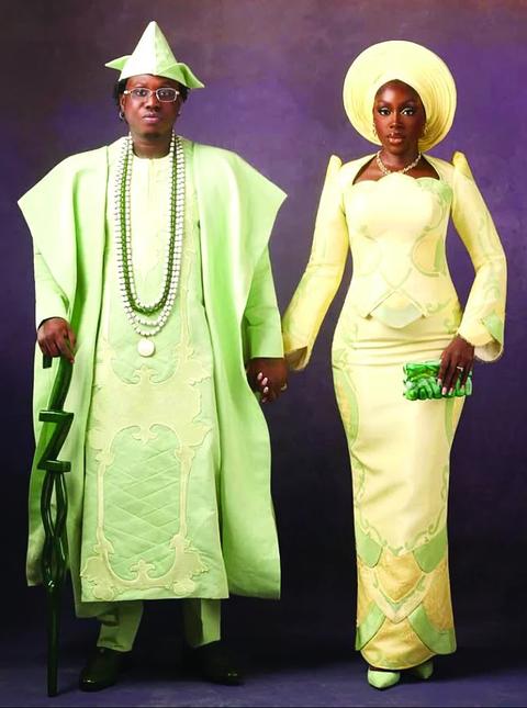 full-length studio shot of groom and bride in pale green aso-oke holding hands