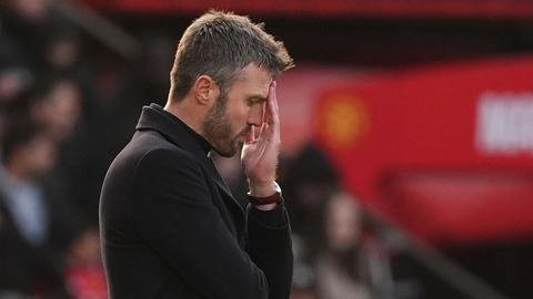 Manager with head in hand, eyes closed, dejected against blurred red stand