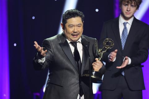Man holding an Emmy statuette while another man claps behind him