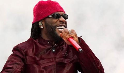 Burna Boy performing in a red hat and sunglasses with a red microphone