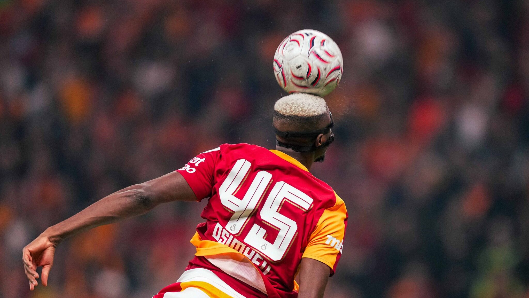 Osimhen seen from behind, number 45 shirt, balancing the ball on his head