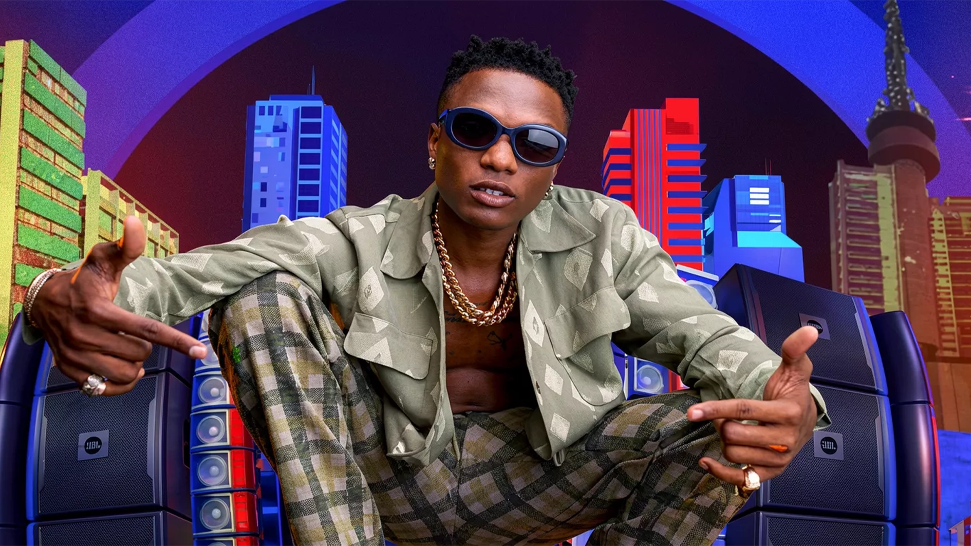 Wizkid seated in front of a colourful city backdrop and speaker stacks