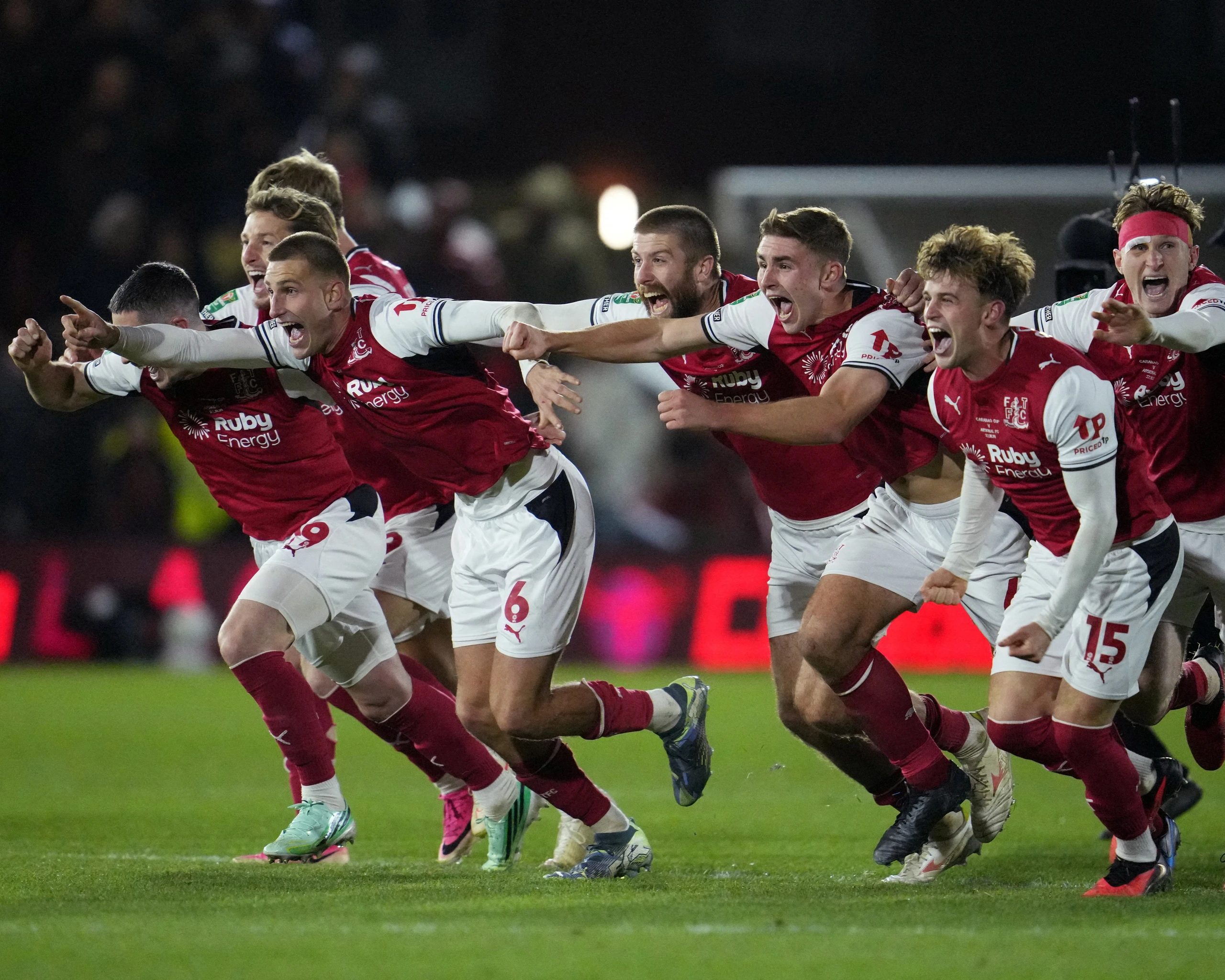 Fleetwood Town players in red and white kits sprinting away in wild celebration