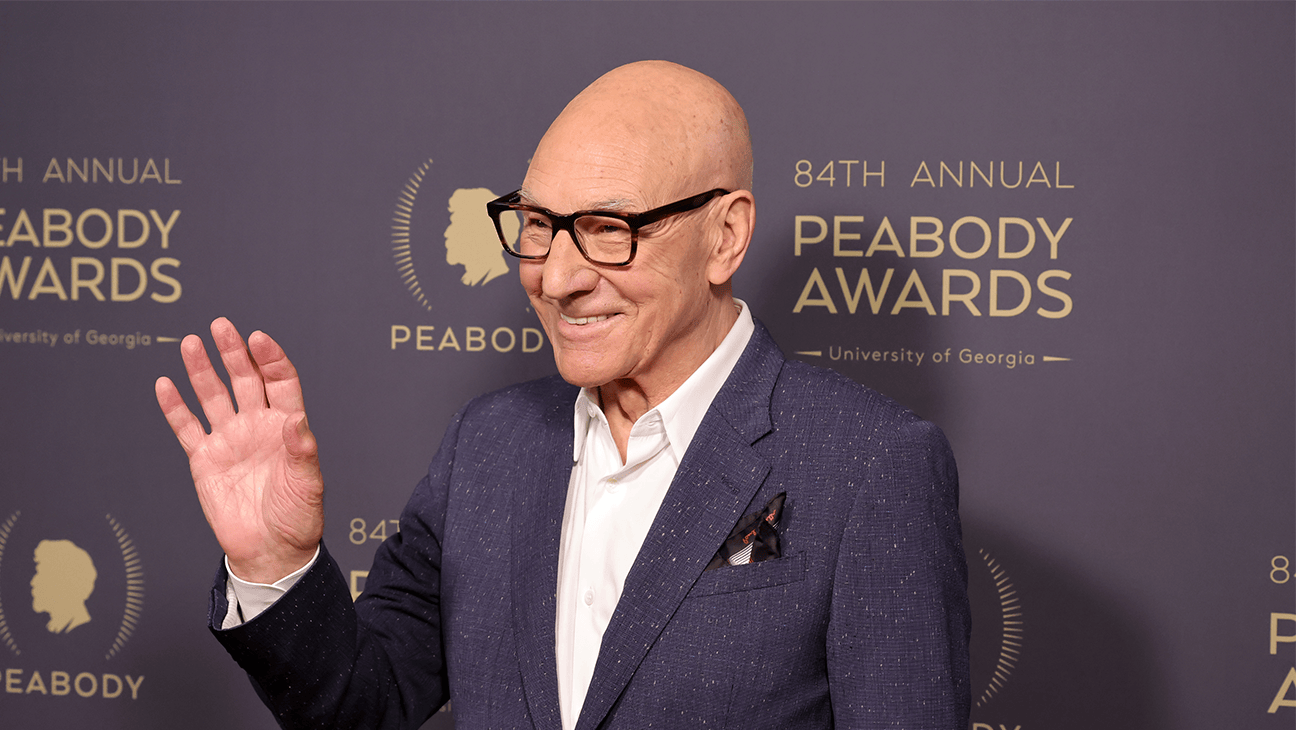 Patrick Stewart in glasses waving in front of a Peabody Awards step-and-repeat backdrop