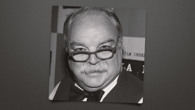 black-and-white portrait of a balding man with glasses and mustache, sign text behind