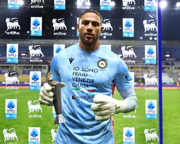 Goalkeeper in light blue kit holding gloves and an award in front of sponsor boards