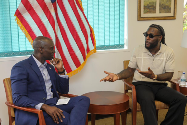 two men talking in an office with a US flag