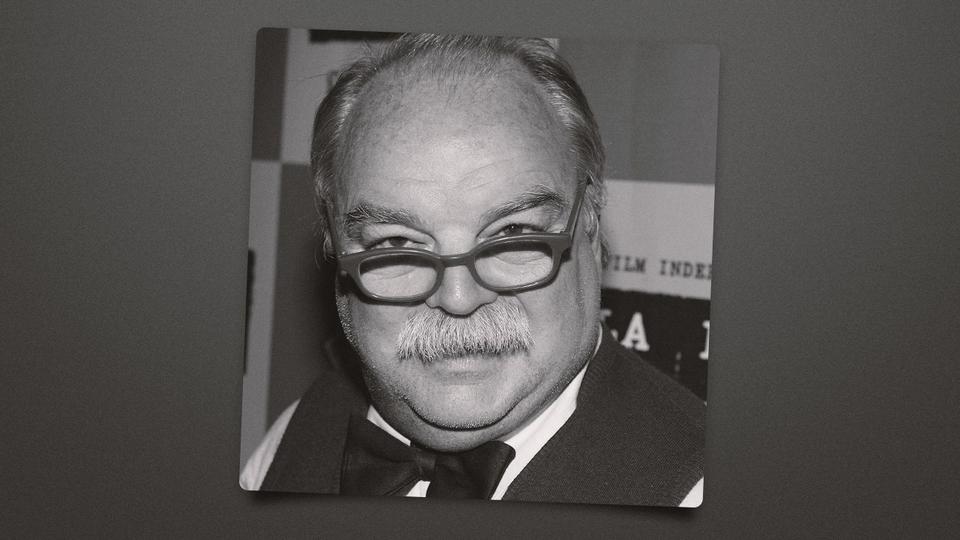 black-and-white portrait of a balding man with glasses and mustache, sign text behind