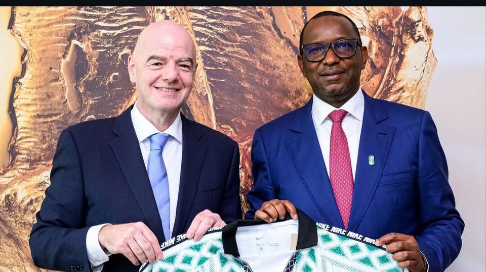 Two officials in suits holding up a Nigeria national team shirt; kit sponsor marks on the jersey are part of the scene