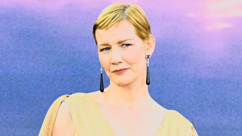 woman with short blonde hair and long earrings against a blue backdrop