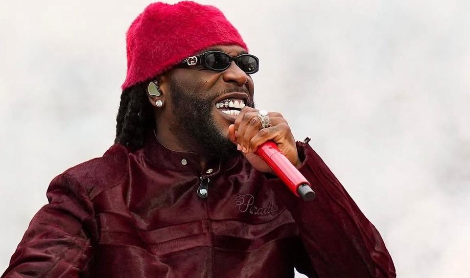 Burna Boy performing in a red hat and sunglasses with a red microphone