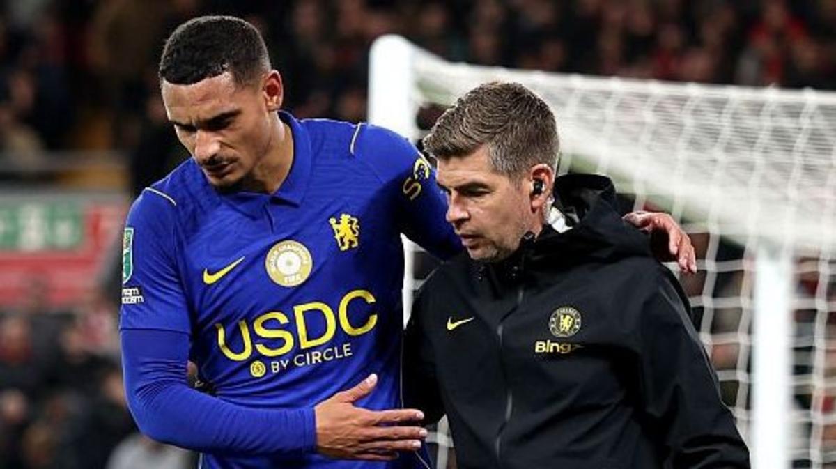 Maxence Lacroix in Chelsea blue walking off injured, helped by a member of Chelsea staff; kit sponsor marks are part of 